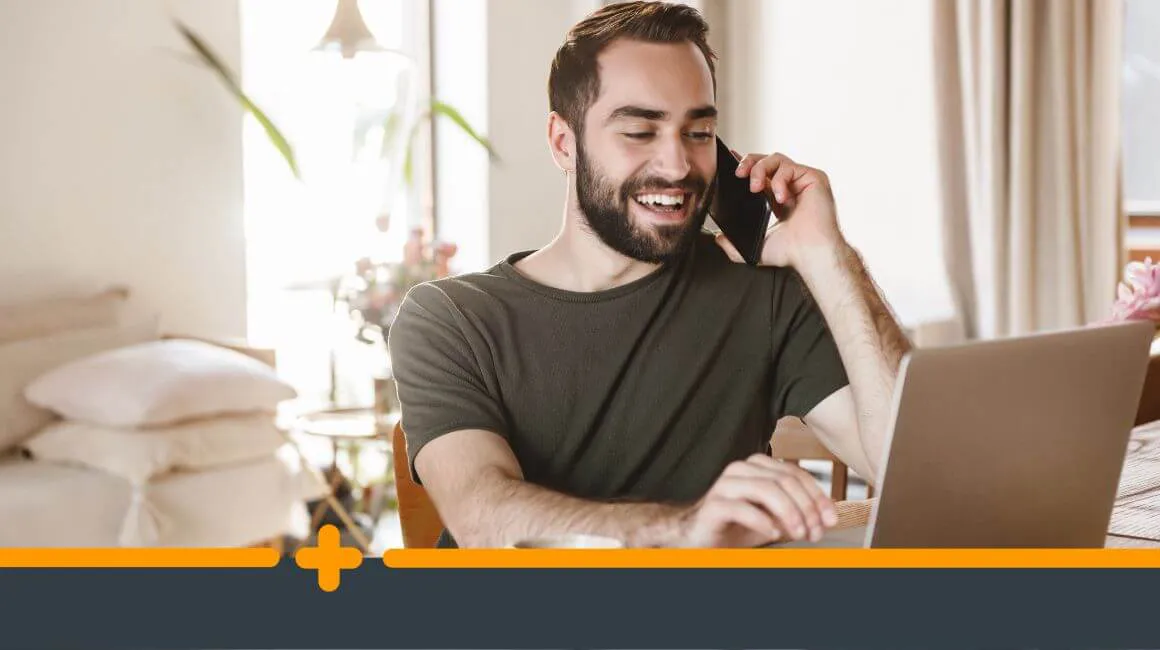 Zadowolony mężczyzna rozmawiający przez telefon i korzystający z laptopa w domowym biurze