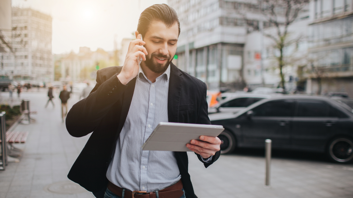 Mężczyzna w garniturze rozmawia przez telefon i przegląda dokumenty na tablecie podczas spaceru po mieście